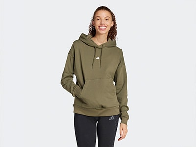A young woman with curly hair is wearing a green hooded sweatshirt and smiling at the camera against a plain white background.