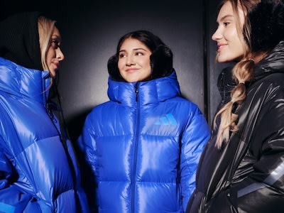 La imagen muestra a tres mujeres jóvenes con chaquetas acolchadas de colores sobre un fondo oscuro.