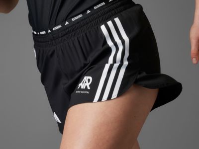 Snímka zblízka odhaľuje spodnú časť tela človeka v čiernych športových šortkách s bielymi prúžkami a výrazným logom "Adidas".