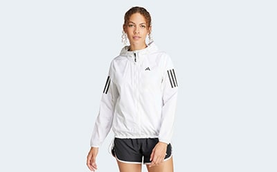 A woman wearing a white athletic jacket with black stripes stands against a plain white background.