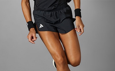 The image shows a person wearing black athletic shorts and a black top, with their legs and arms visible against a plain gray background.