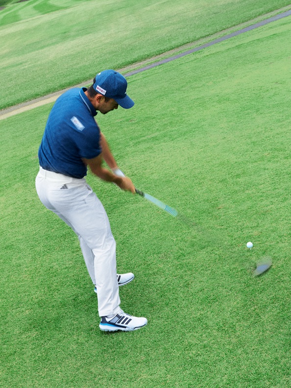 A person in a blue shirt and cap is swinging a golf club on a lush green golf course.