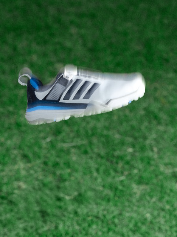 A white and blue athletic shoe rests on a lush, green grassy surface.