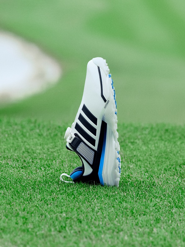 A white and black athletic shoe with blue accents sits on a lush green grass field.