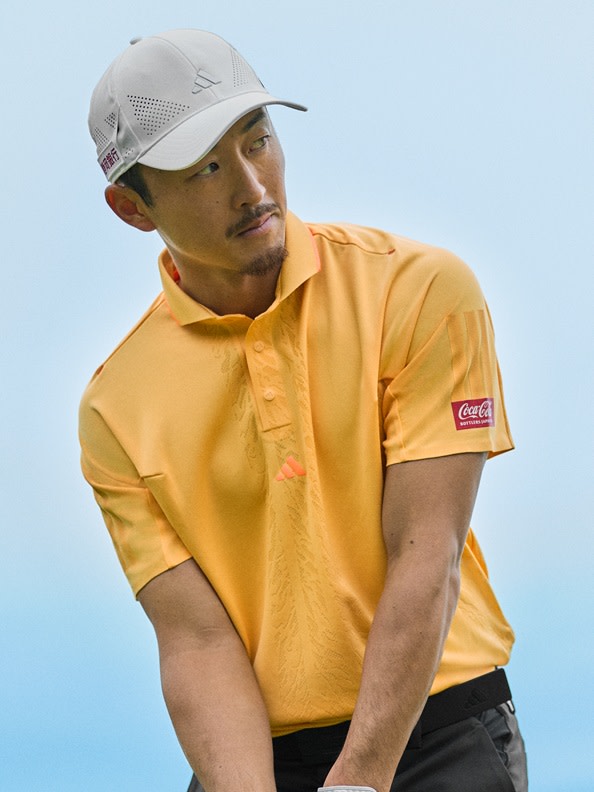 A person wearing a yellow shirt and a gray baseball cap stands against a clear blue sky background.