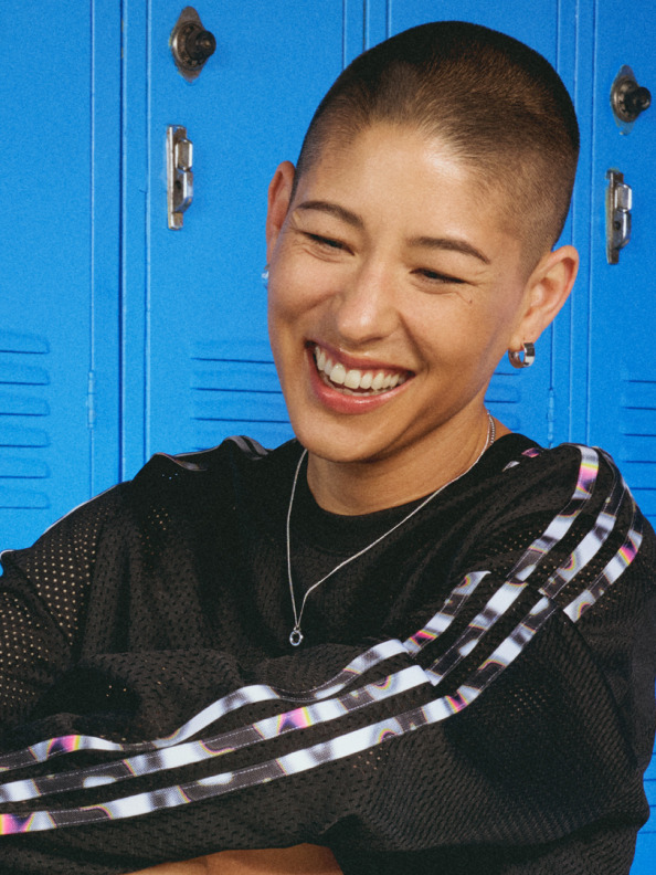 A woman with a shaved head smiles in a black adidas x Pabllo Vittar top.