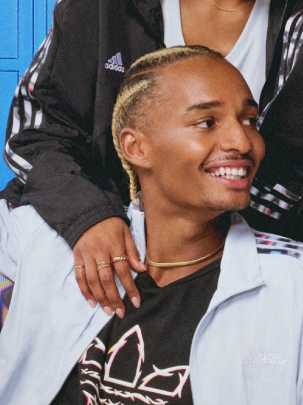 A man with blonde braids smiles in a grey adidas x Pabllo Vittar hoodie. 
