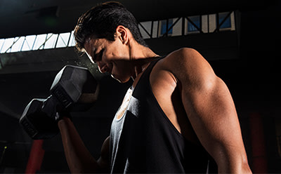 A shirtless individual stands in a dimly lit room, their face obscured as they appear to be engaged in some form of physical activity or exercise.