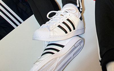 A pair of white sneakers with black stripes sits on a white and black background, showcasing the distinctive design and features of the athletic footwear.