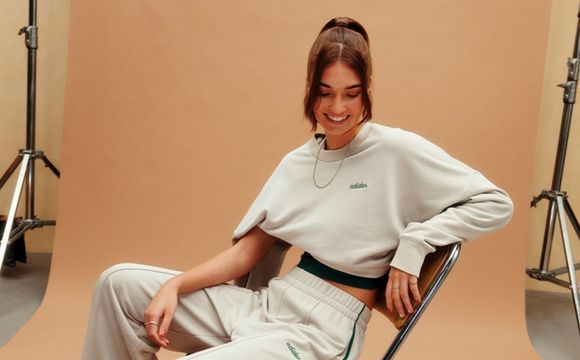 The image shows a smiling young woman wearing a white sweater and sitting in a chair against a plain beige background.