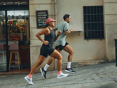 Two people, a man and a woman, are jogging together on a city street, with storefronts and buildings visible in the background.