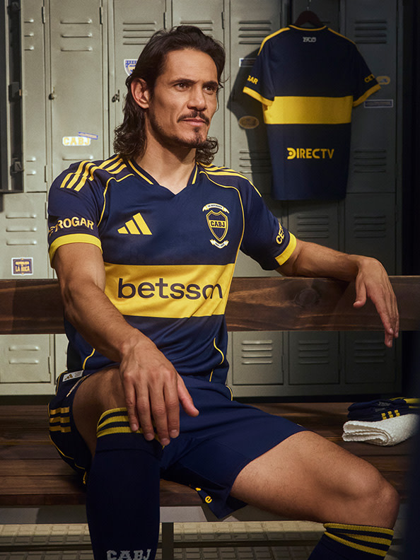 The image shows a man wearing a blue and yellow soccer jersey, sitting on a bench in front of lockers.