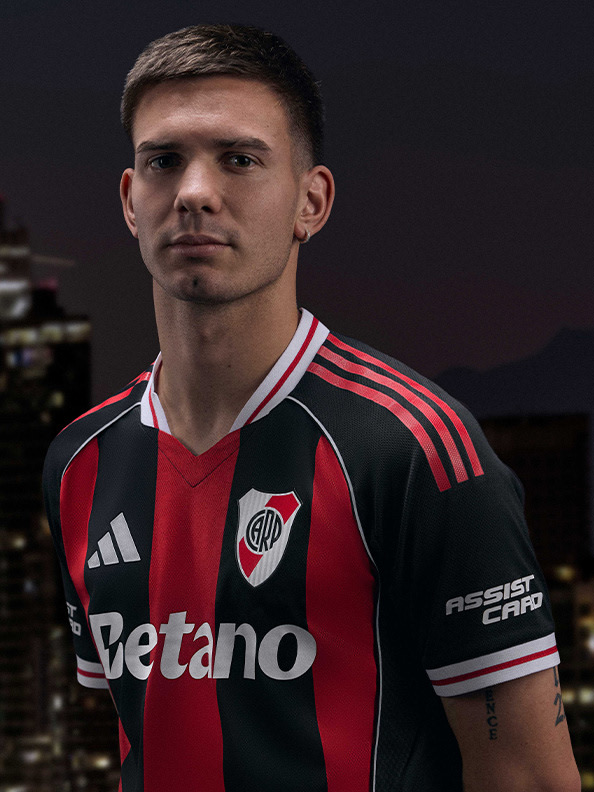 The image shows a young man wearing a red and black soccer jersey, standing in front of a dark background.