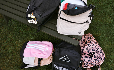The image shows various personal items, including a backpack, a pink towel, and a leopard-print scarf, placed on a grassy surface.