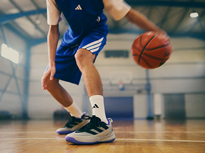 A basketball player in a blue jersey dribbling an orange basketball on a wooden court in a sports hall.