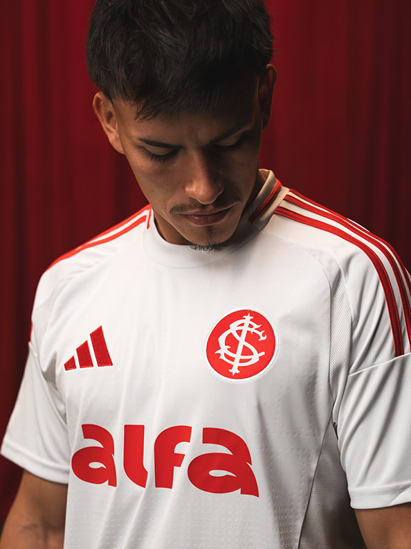 A young man wearing a white and red sports jersey with the text "Alfa" stands in front of a red background.