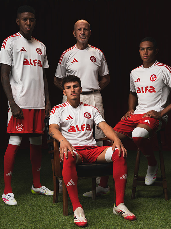 The image shows a group of four individuals wearing white and red sports uniforms, posing together on a dark background.