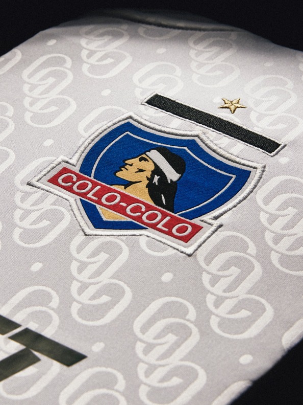 The image shows the logo of the Colo-Colo football club, a prominent Chilean soccer team, prominently displayed on a white jersey or uniform with a repeating pattern in the background.