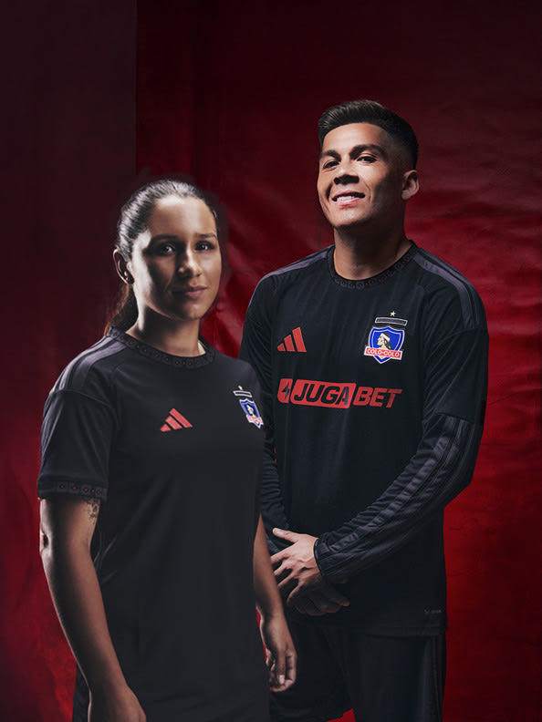 The image shows two people, a woman and a man, wearing black sports jerseys with the "Juga Bet" logo, standing in front of a red background.