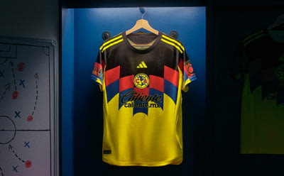 A yellow and black soccer jersey with red and black accents is displayed on a hanger against a blue background.