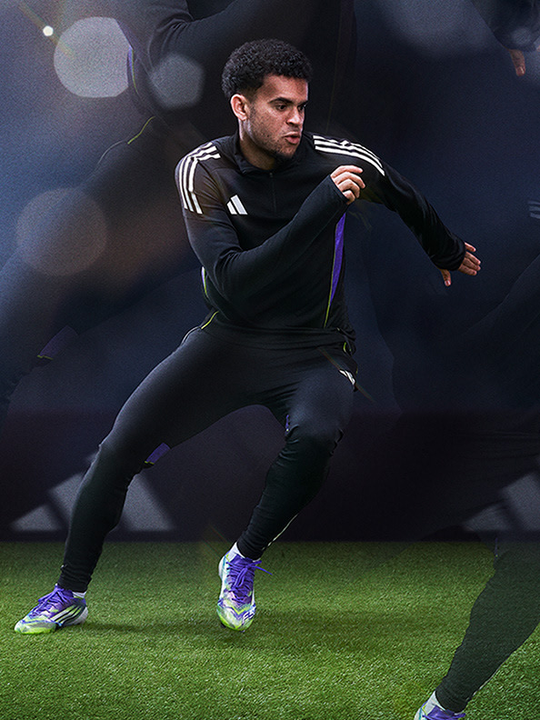 A person in a black athletic outfit is running on a grassy field with a blurred background of lights.
