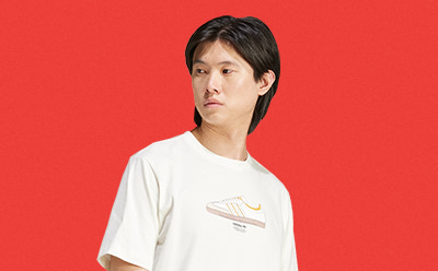 A person with short dark hair wearing a white t-shirt stands against a bright red background.
