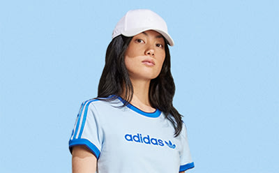A young person wearing an Adidas shirt and a white hat, standing against a blue background.