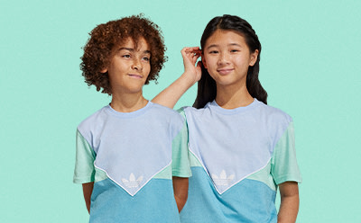 Two young individuals, one with curly brown hair and the other with straight black hair, are standing together against a teal background, wearing matching light blue and white shirts.