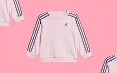 Una sudadera adidas de color blanco con tres bandas negras en las mangas sobre un fondo rosa.
