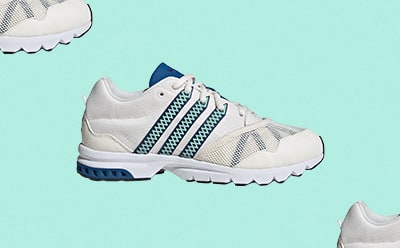 Witte en blauwe sportschoenen met textuur op de zool tegen een mintgroene achtergrond.