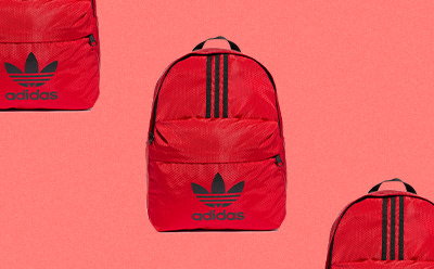 Een rode adidas rugzak met het iconische 3-Stripes logo van het merk, prominent zichtbaar tegen een levendige rode achtergrond.