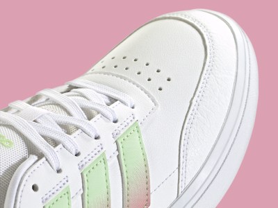 Primer plano de zapatilla blanca con detalles verdes y rosas sobre un fondo rosa.