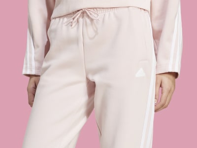 Un pantalón de color rosa claro con rayas blancas en los laterales, sobre un fondo liso de color rosa.