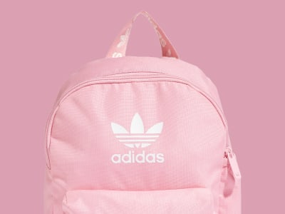 Una mochila adidas rosa con el icónico logotipo de la marca sobre un fondo rosa liso.