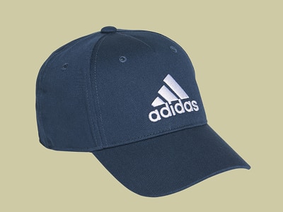 Una gorra de béisbol adidas en azul marino con el icónico logotipo de adidas sobre un fondo beige claro.