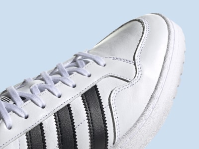 Primer plano de zapatilla blanca con bandas negras sobre un fondo azul claro.