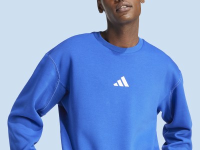 Una persona con una sudadera azul de adidas está de pie frente a un cielo azul claro.