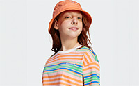 A young person with red hair wearing an orange hat and a colorful striped shirt stands against a plain white background.