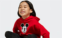 A young girl wearing a red Mickey Mouse hoodie is smiling and making a funny face against a plain white background.