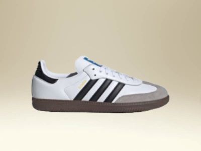 A pair of white and black sneakers with a gum sole is displayed against a beige background.