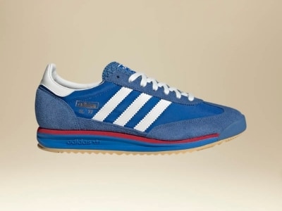 A pair of blue and white Adidas sneakers with red accents, set against a beige background.