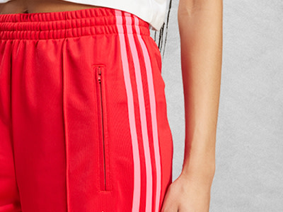 Nahaufnahme des unteren Rumpfs einer Person in leuchtend roten sportlichen Shorts mit weißen Streifen vor einem schlichten weißen Hintergrund.