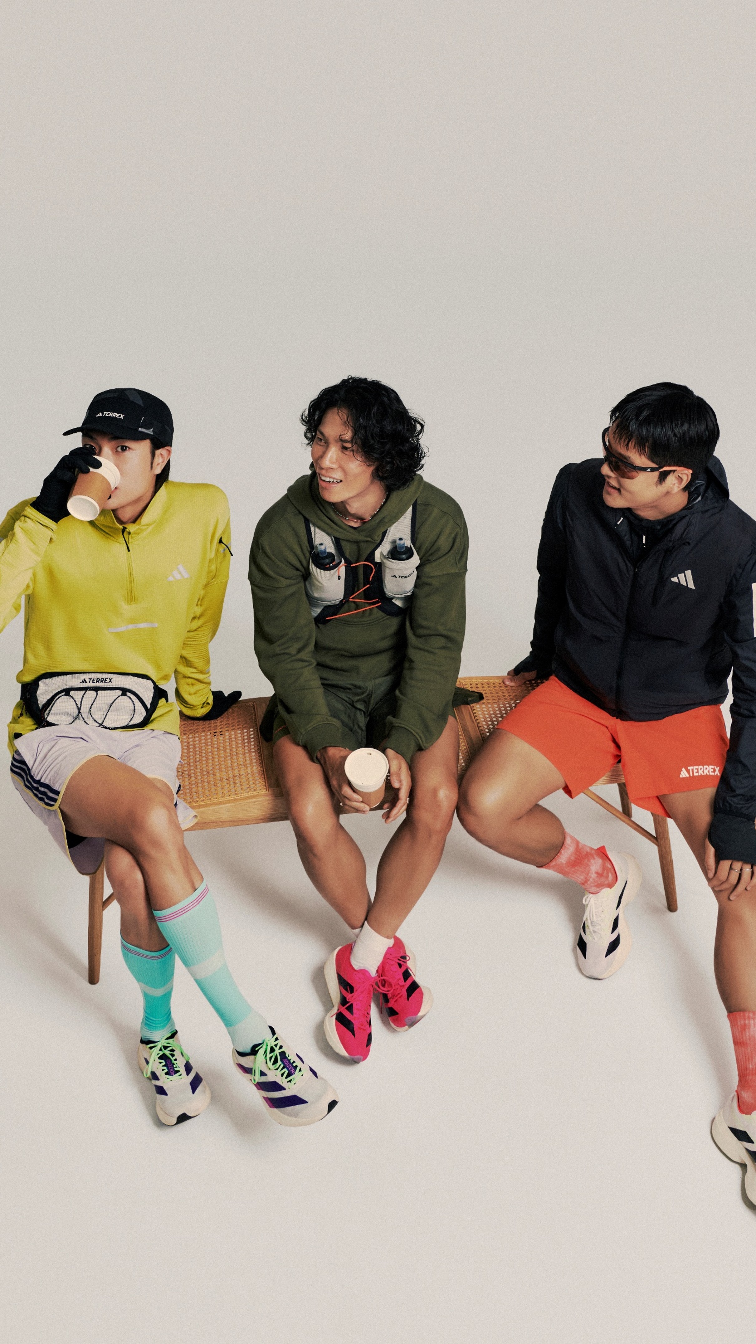 Three individuals, two women and one man, are seated on chairs against a plain background. They are wearing casual clothing, including a yellow top, a green jacket, and colorful socks.