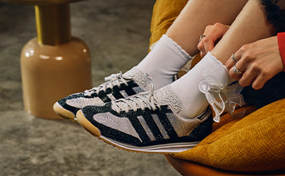 The image shows a person's legs and feet wearing a pair of patterned sneakers, with a glass bottle in the background.