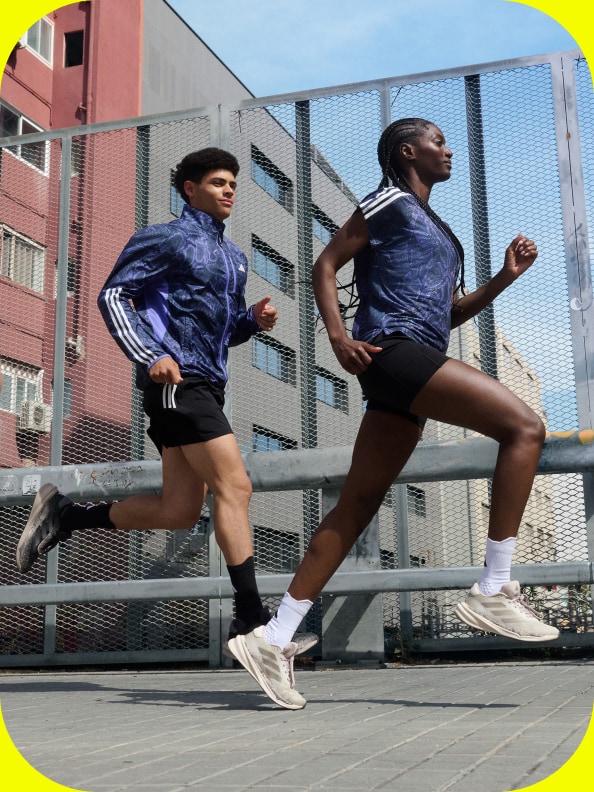 Two people in adidas Running gear are running on a footpath in the city.