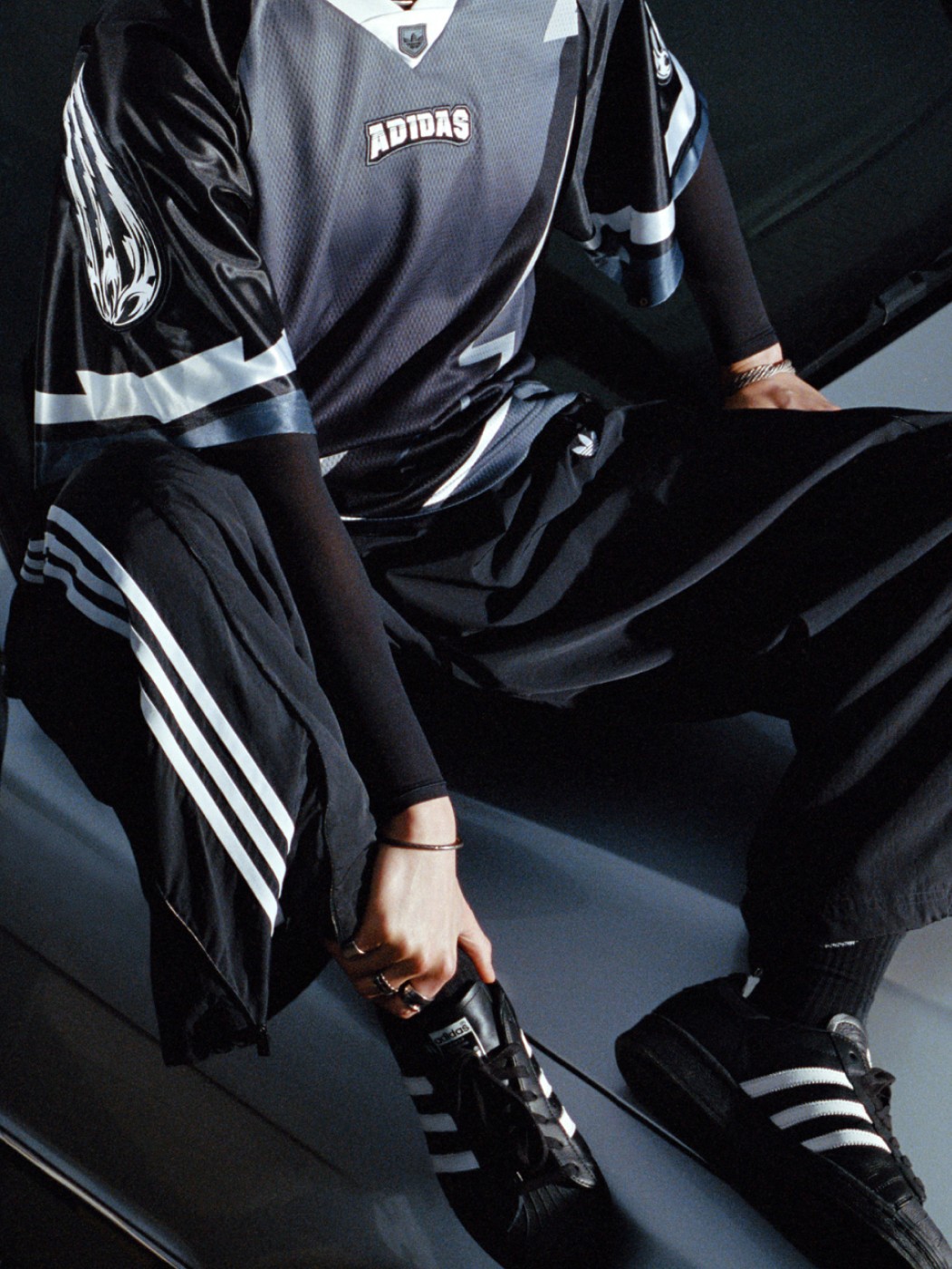 The image shows a person wearing a black and white Adidas sports jersey and pants, sitting on a dark surface with their hands on their knees.