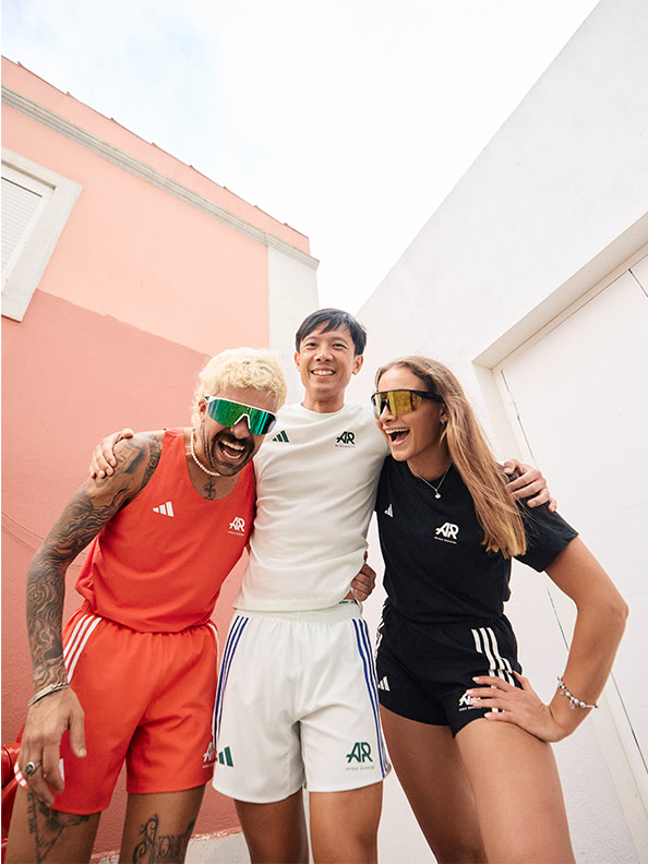 Three people, two men and one woman, standing with their arms around each other laughing and smiling