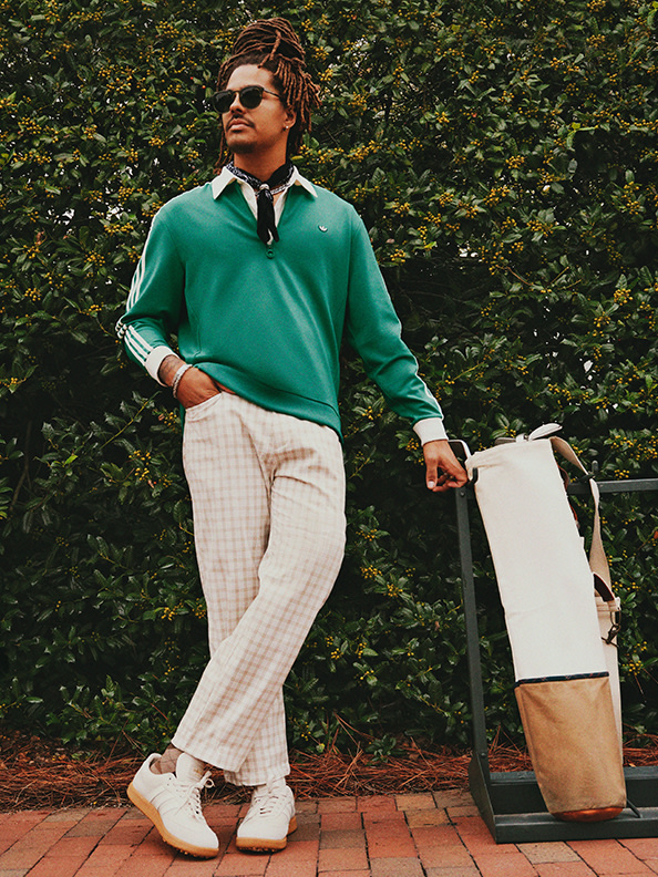 Man in green sweater holding a golf bag. 