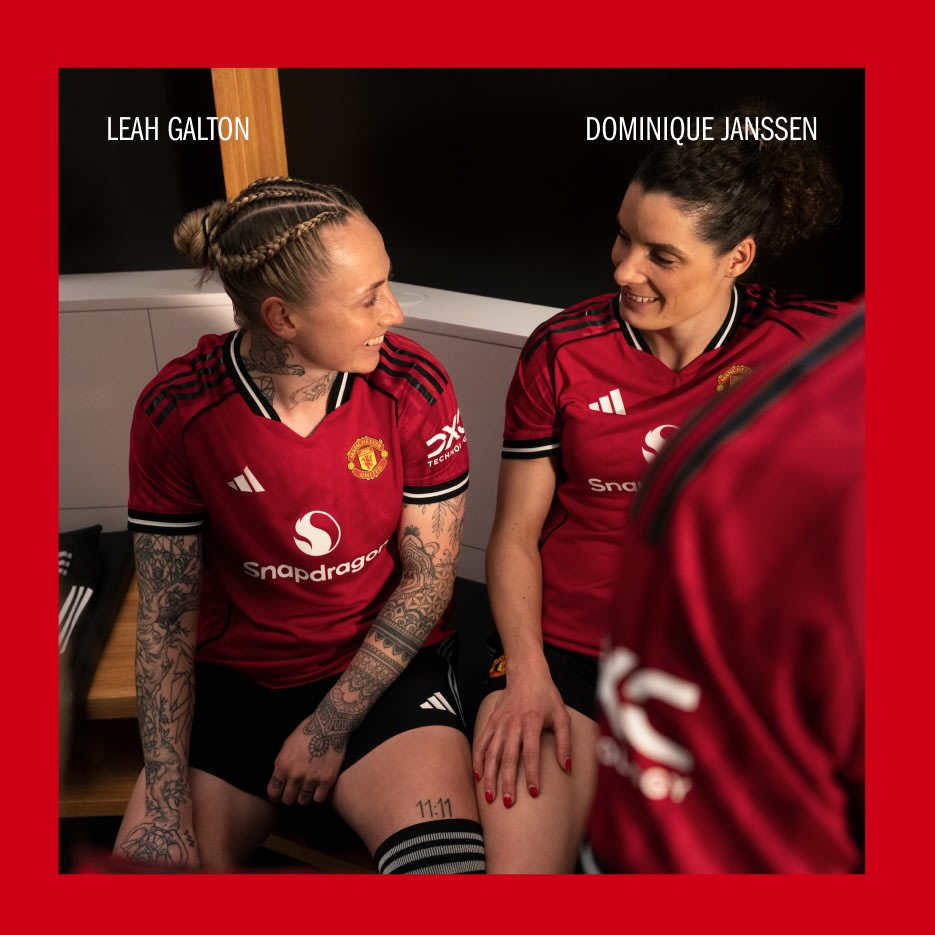 Dos personas vestidas con camisetas de fútbol del Manchester United están sentadas juntas, con un fondo rojo.