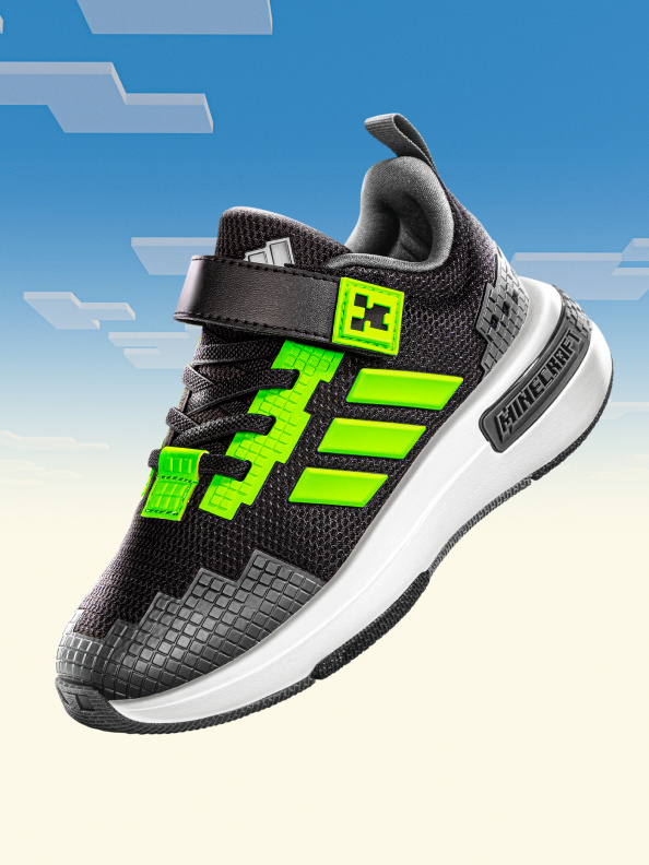 รองเท้ากีฬาสีเขียวดำพร้อมพื้นรองเท้าที่มีผิวสัมผัสและโลโก้สะดุดตาด้านข้างที่โดดเด่นตัดกับท้องฟ้าสีสดใสที่มีเมฆดงาม